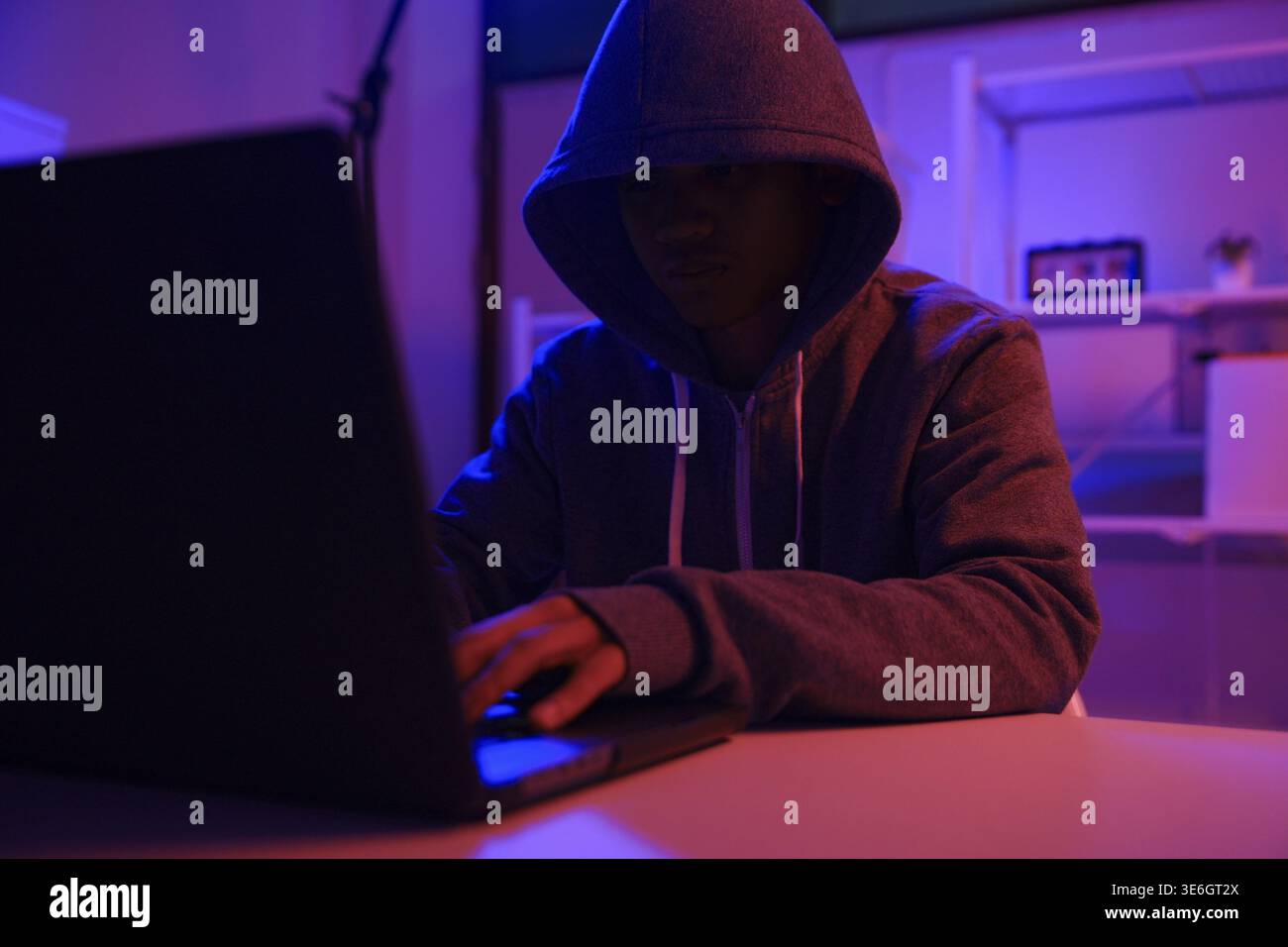 A mysterious hooded hacker working on a computer in a dark room. A concept for cybersecurity, hacking, cybercrime, and data privacy threats Stock Photo