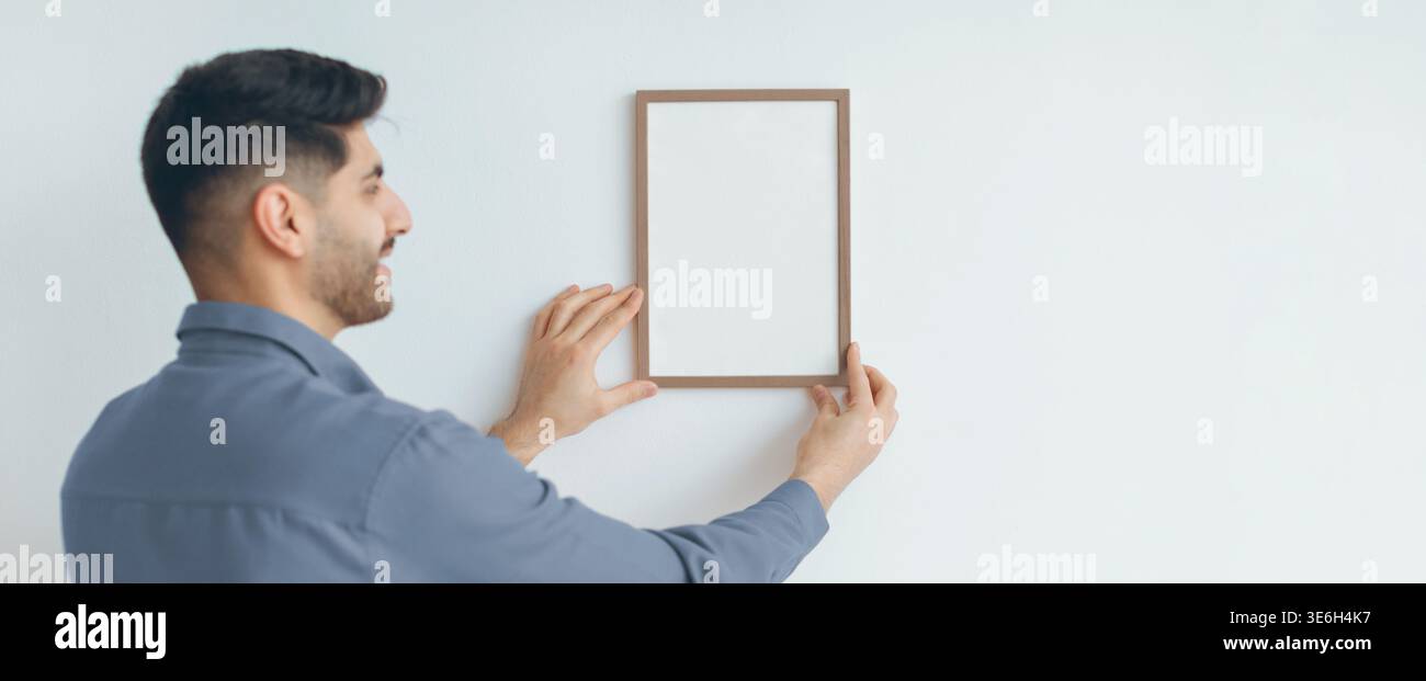 Man Holds Empty Frame on Wall While Smiling During Home Decoration Activity at Daytime Stock Photo