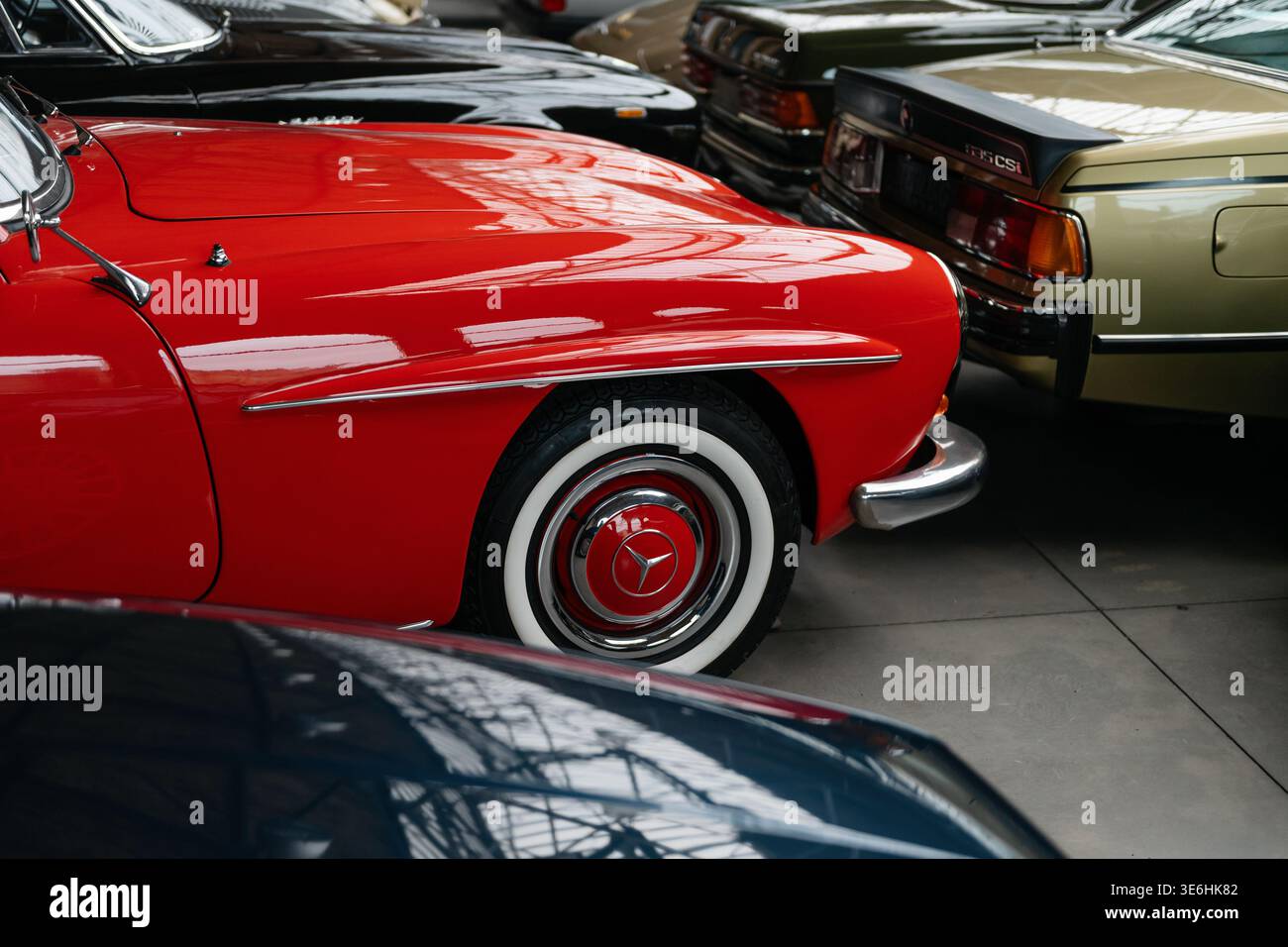 Classic Mercedes-Benz with whitewall tires in car collection. A front part of red Mercedes-Benz 190SL parked alongside a BMW 635CSi and other old cars Stock Photo