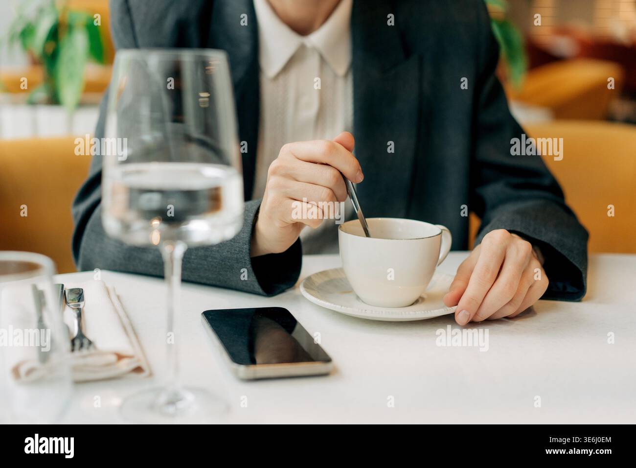 Close-up of an unrecognizable woman's hands placing sugar in coffee in a restaurant while her mobile phone lies nearby on the table. Stock Photo