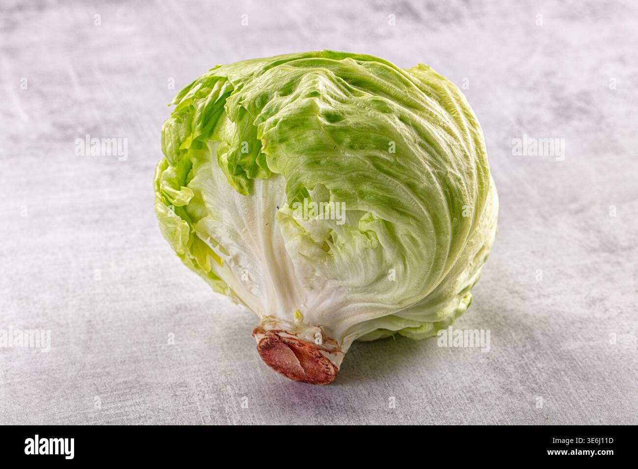 A single head of crisp green iceberg lettuce on a textured gray ...