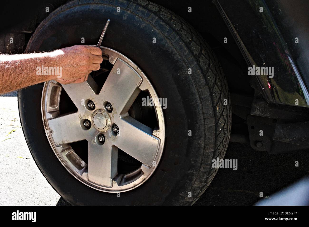 A person's hand uses a tire pressure gauge to check the air in a ...