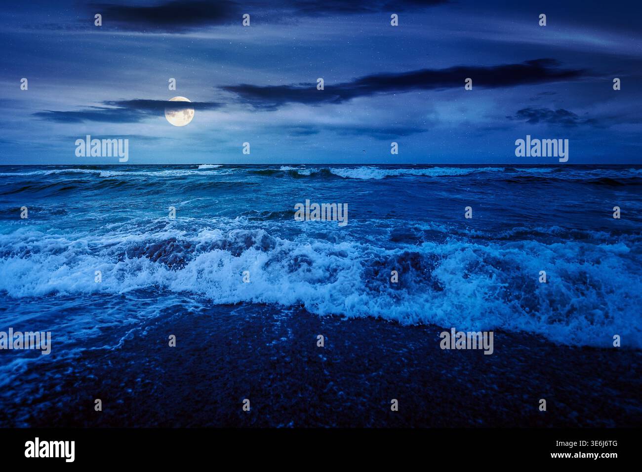 stormy weather on the sandy beach at night. dramatic sky over the sea in full moon light. moody summer landscape. waves crashing the shore. mysterious Stock Photo