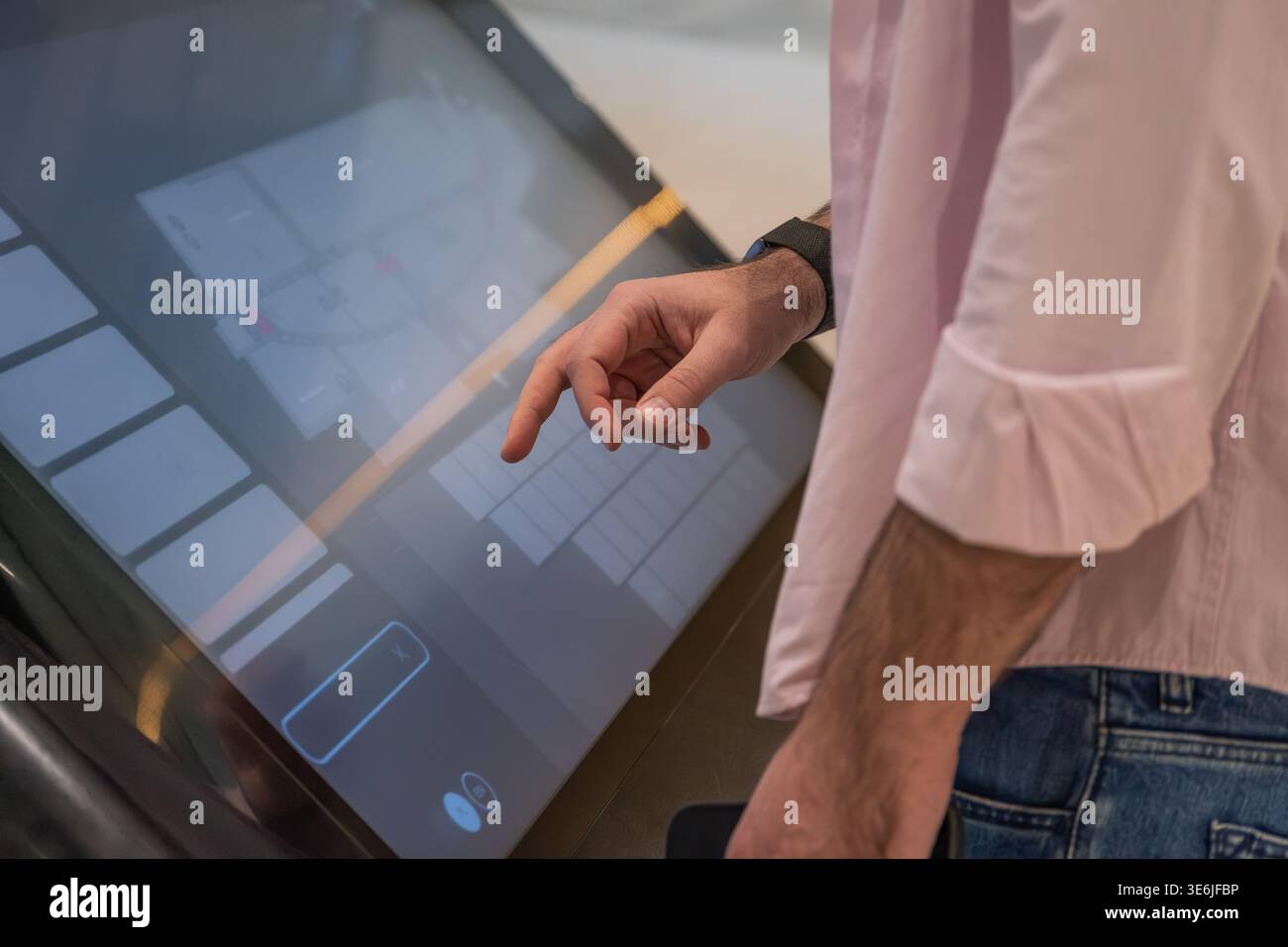 Close view of a man using a touchscreen kiosk interface in a modern indoor environment. Concept of digital technology, self service systems, and user Stock Photo