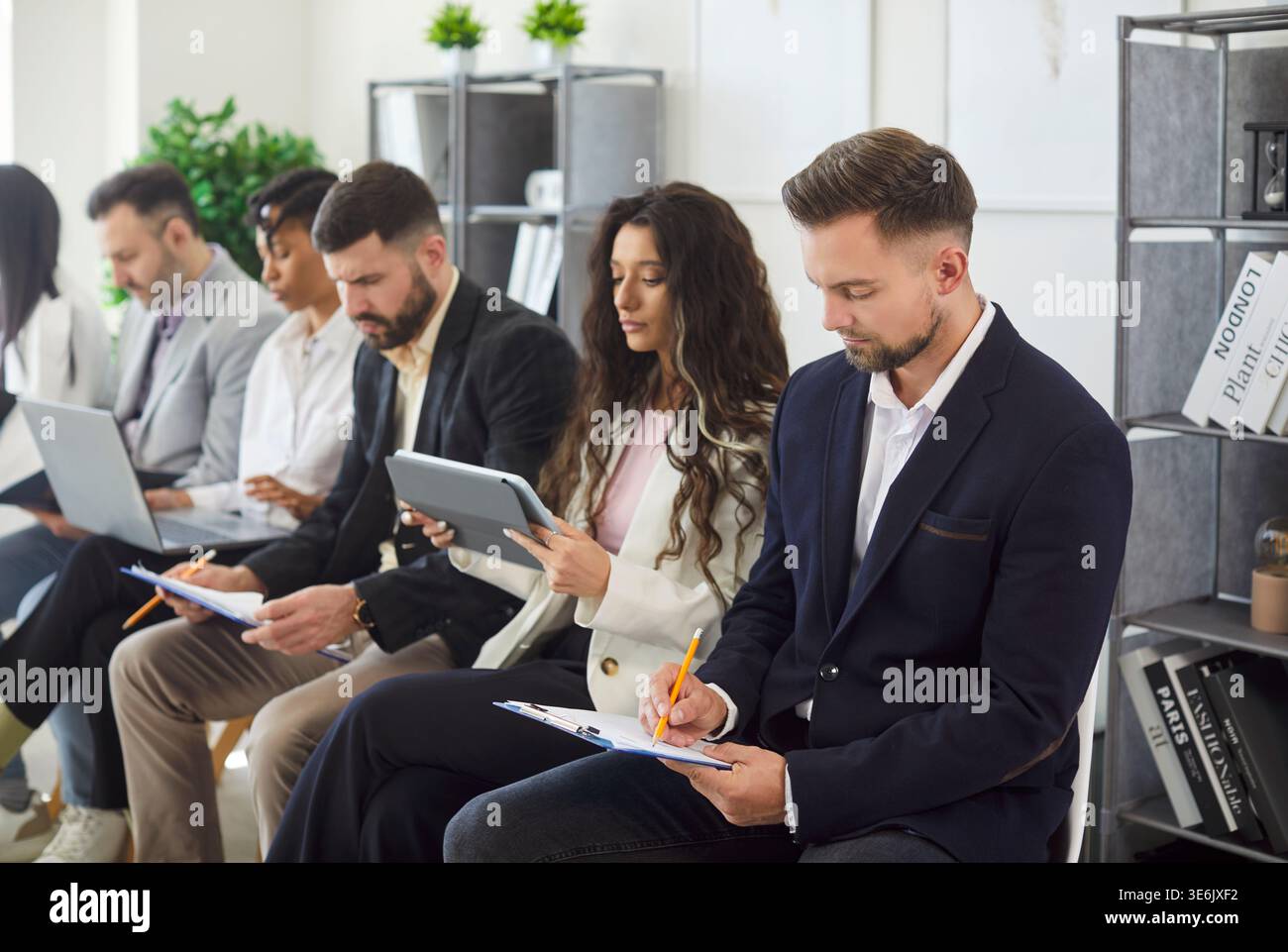 Employees working on devices, making notes seated in row in office Stock Photo