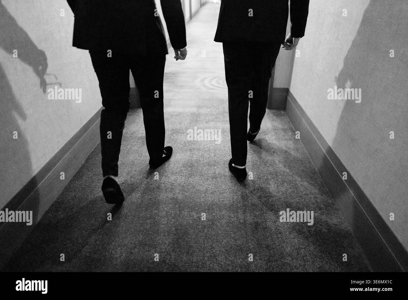 Two Persons Moving Through Corridor With Formal Attire And Dramatic Lighting Stock Photo