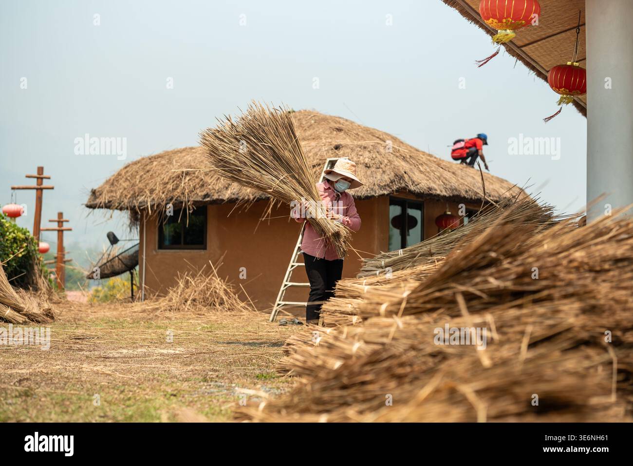 Local workers in Thailand rural village working on house roof repair, covering building using straw. Stock Photo