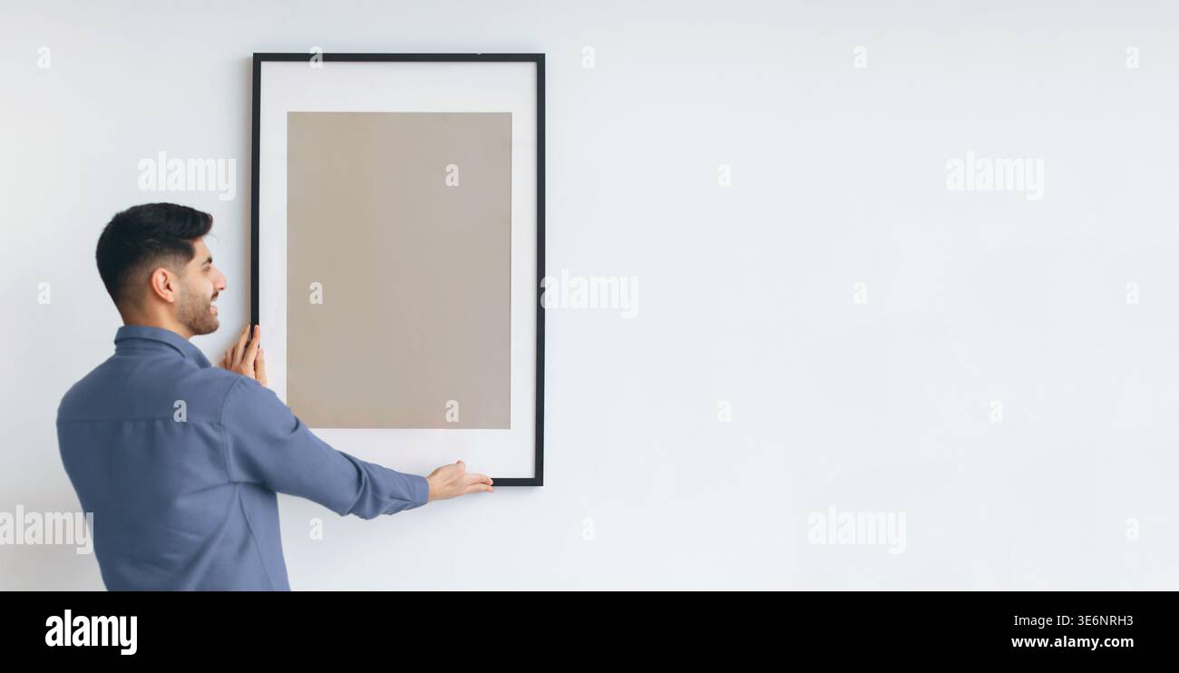 Man Holds Picture Frame on Wall While Preparing for Artwork Placement in a Modern Space Stock Photo