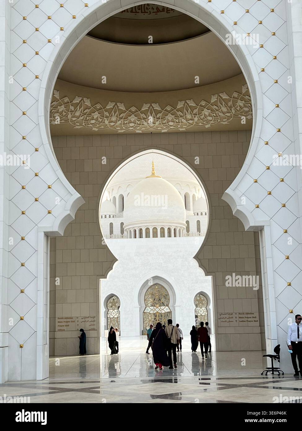 Visitors walking through an arched passage at Sheikh Zayed Grand Mosque in Abu Dhabi, United Arab Emirates. - Smartphone Captured Stock Image