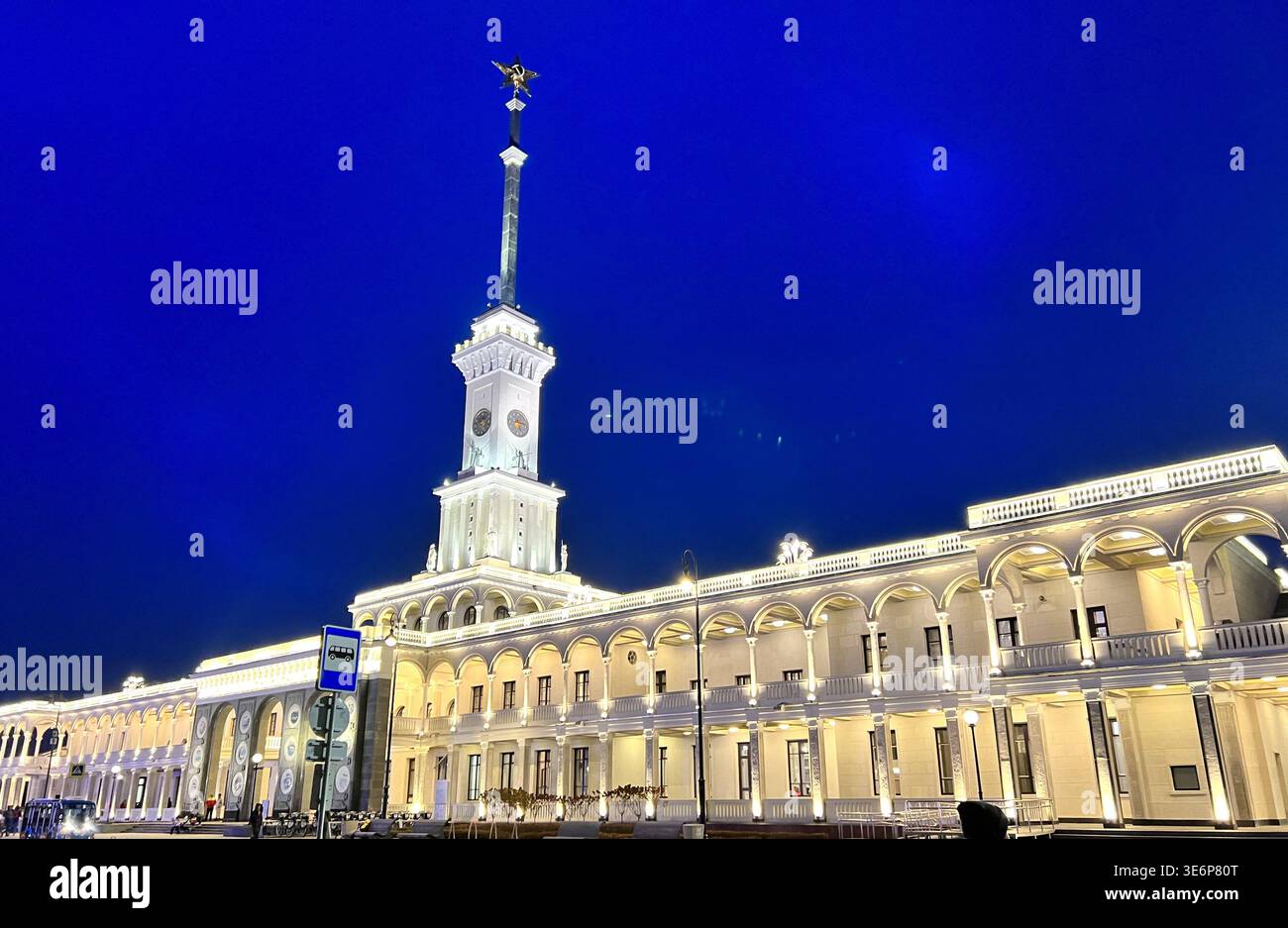 Illuminated North River Terminal building with clock tower and spire at night in Moscow, Russia - Smartphone Captured Stock Image