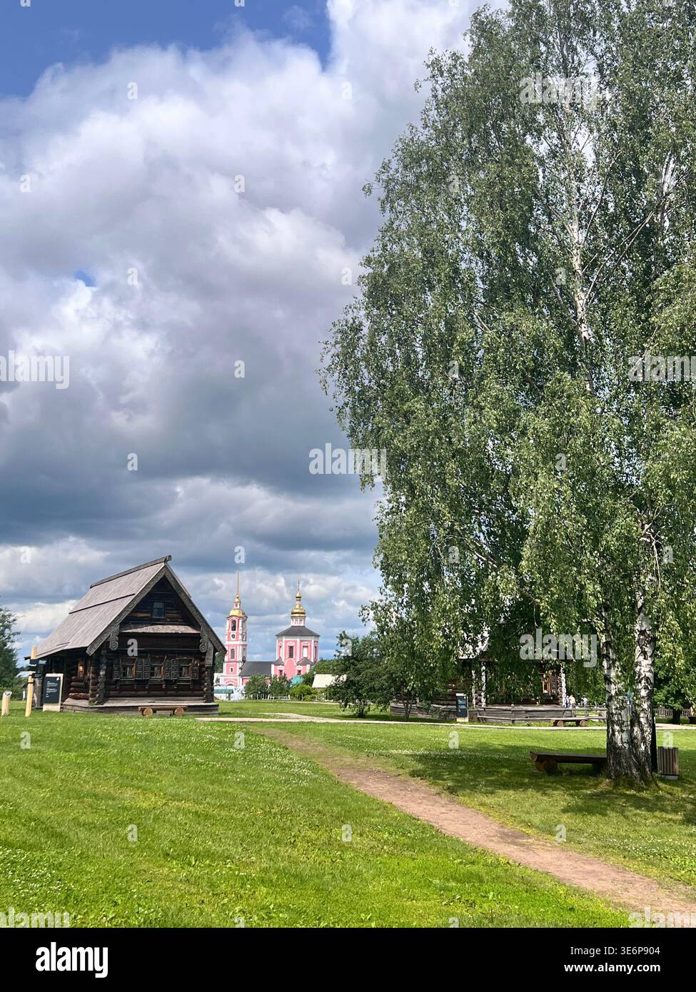 Historic wooden buildings at the Museum of Wooden Architecture in Suzdal, Russia, with church towers visible in the background. - Smartphone Captured Stock Image