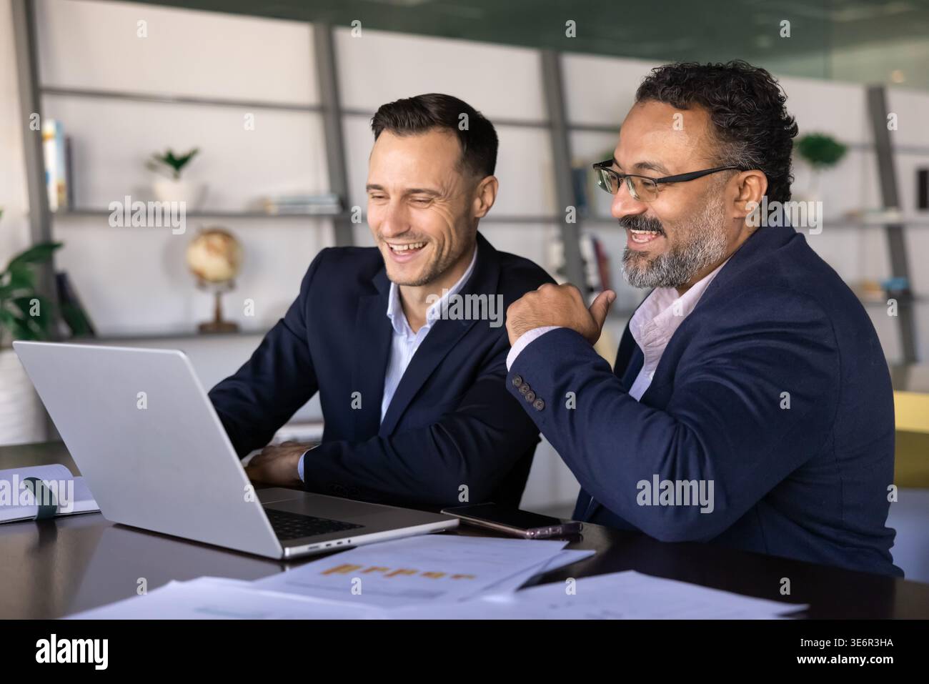 Two businessmen colleagues sit at desk reviewing project result ...