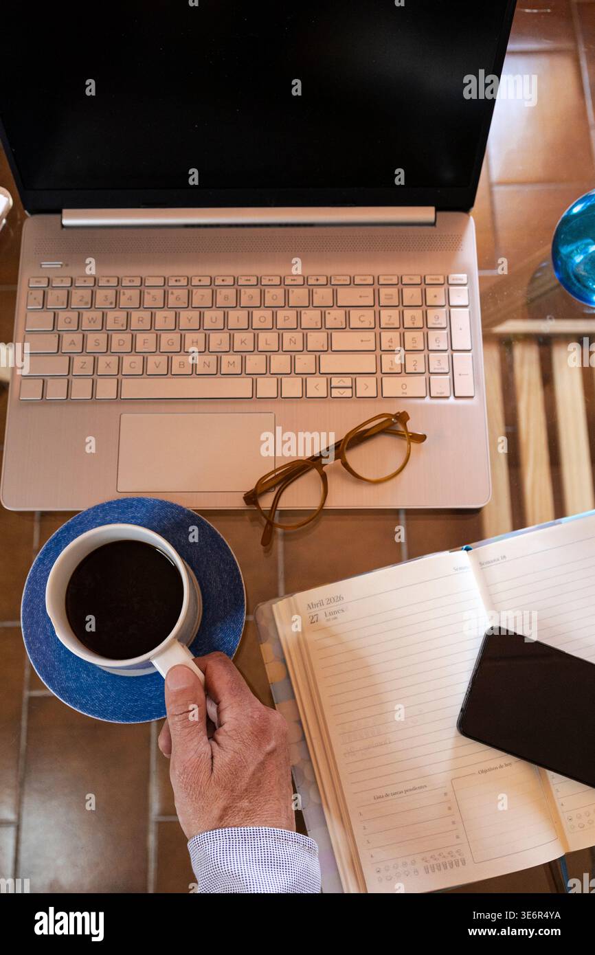 Hand holding coffee while working on laptop with planner and phone at ...