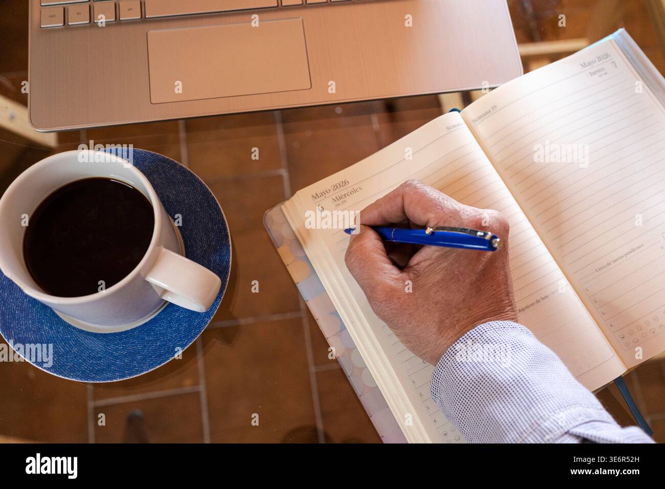 Person writing notes in a planner next to a laptop and coffee Stock ...