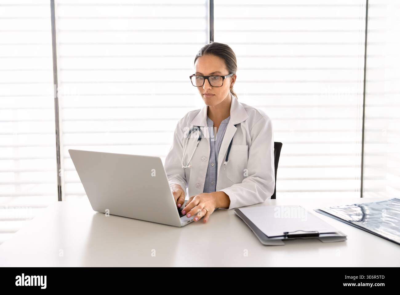 Woman doctor working on laptop at desk in hospital office Stock Photo ...