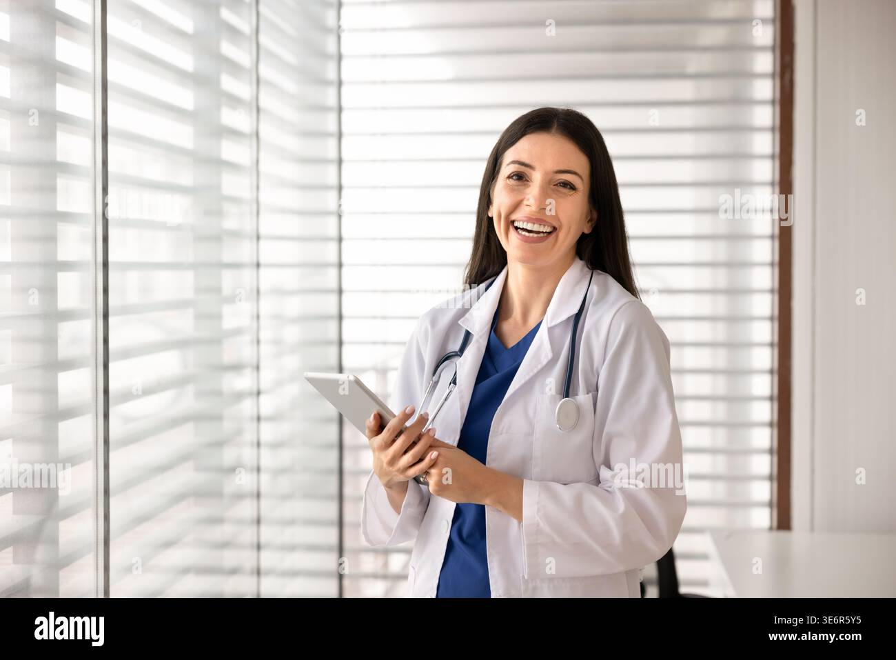 Smiling female doctor in white coat posing in clinic office Stock Photo