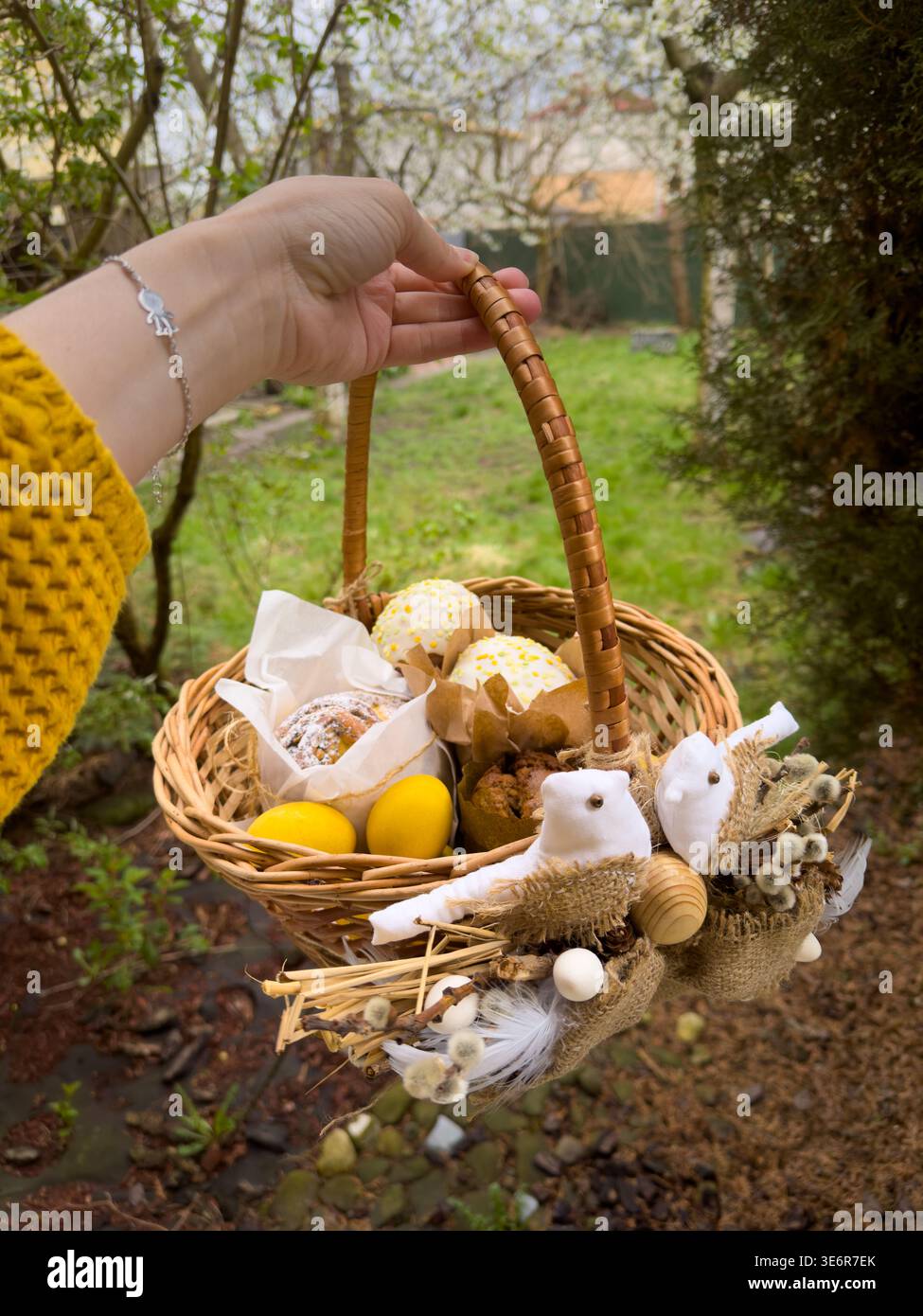 Hand holding rustic easter basket with eggs and treats outdoors Stock Photo