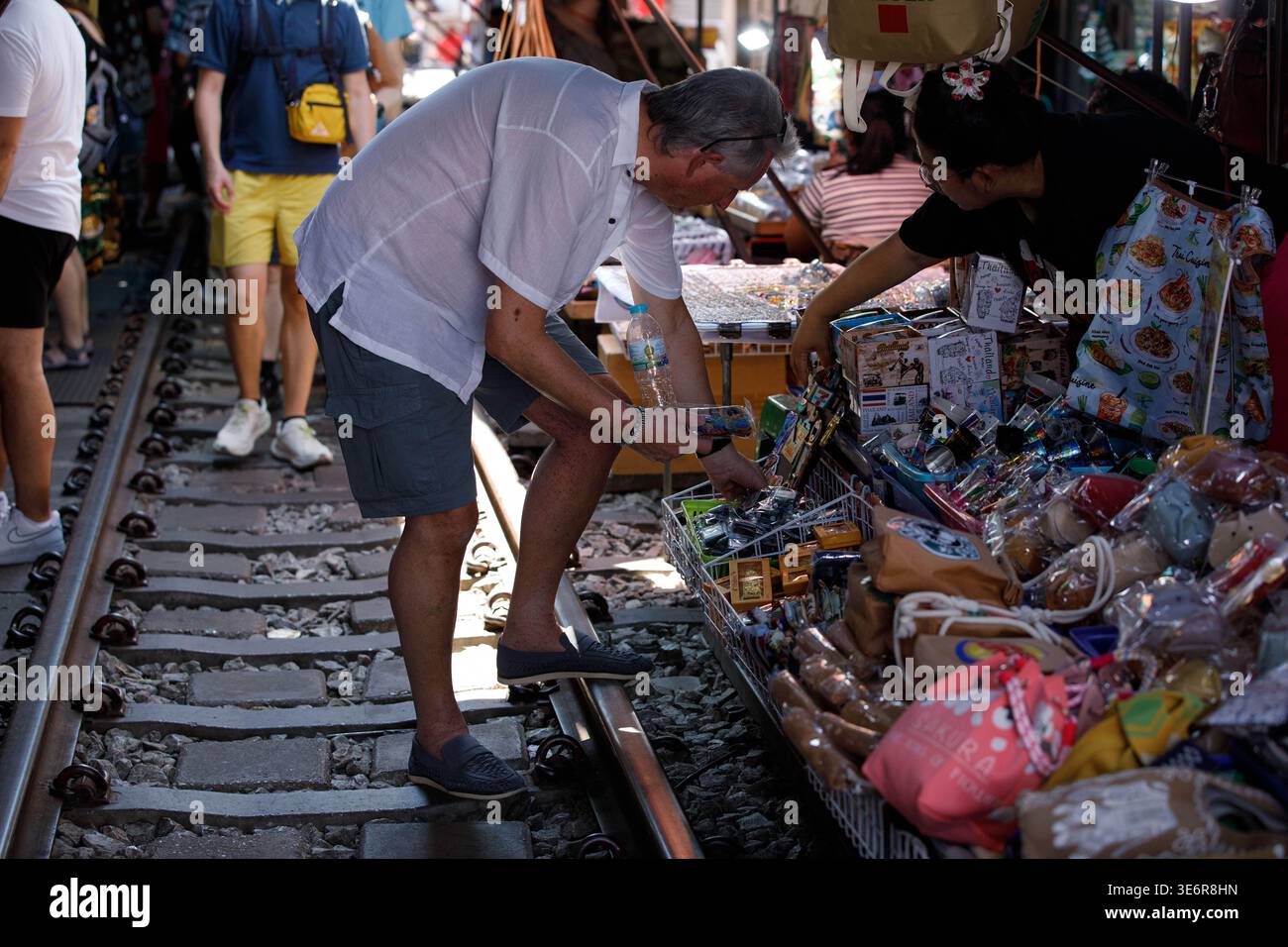SAMUT SONGKHRAM, THAILAND-MAR 28, 2026: Male tourist choosing products at Rom Hub railway market, side profile, Mae Klong Market. Stock Photo