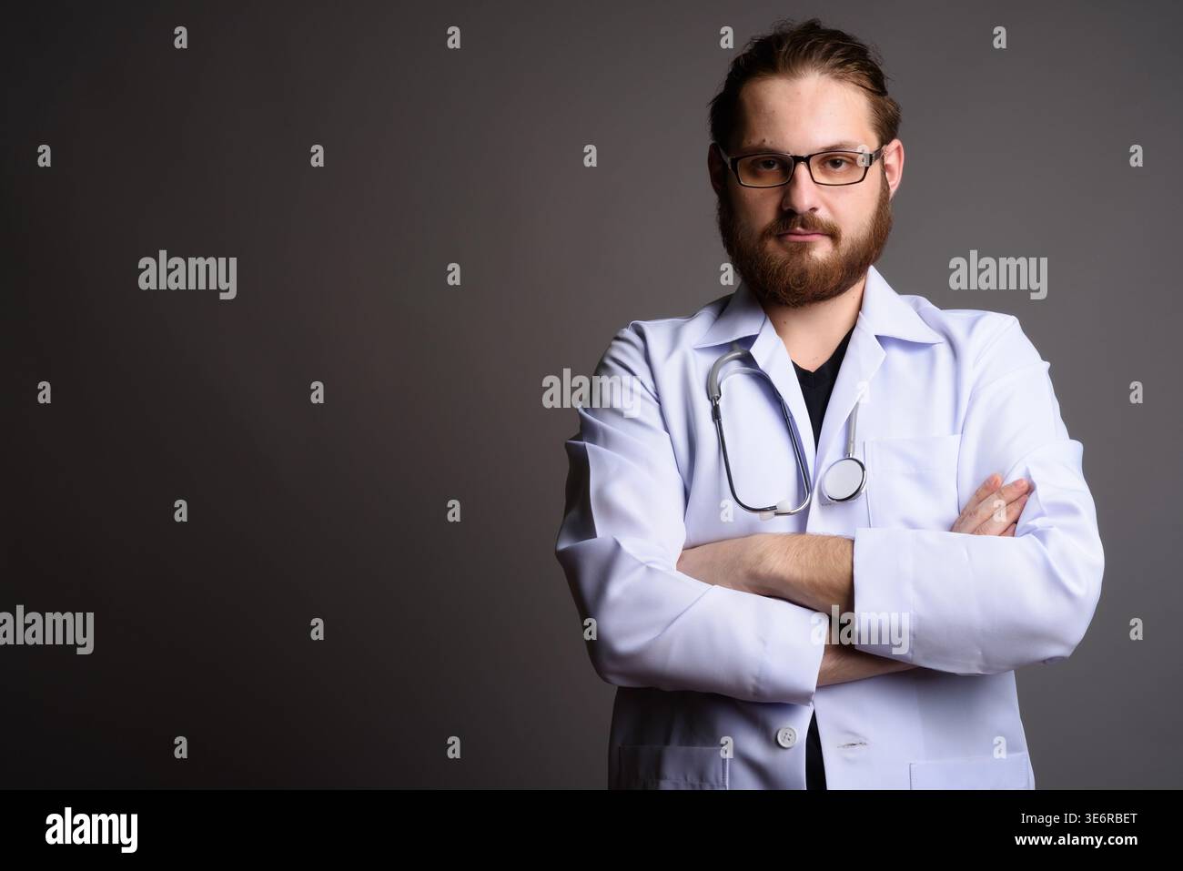Studio portrait of a bearded young male doctor in a white lab coat with ...