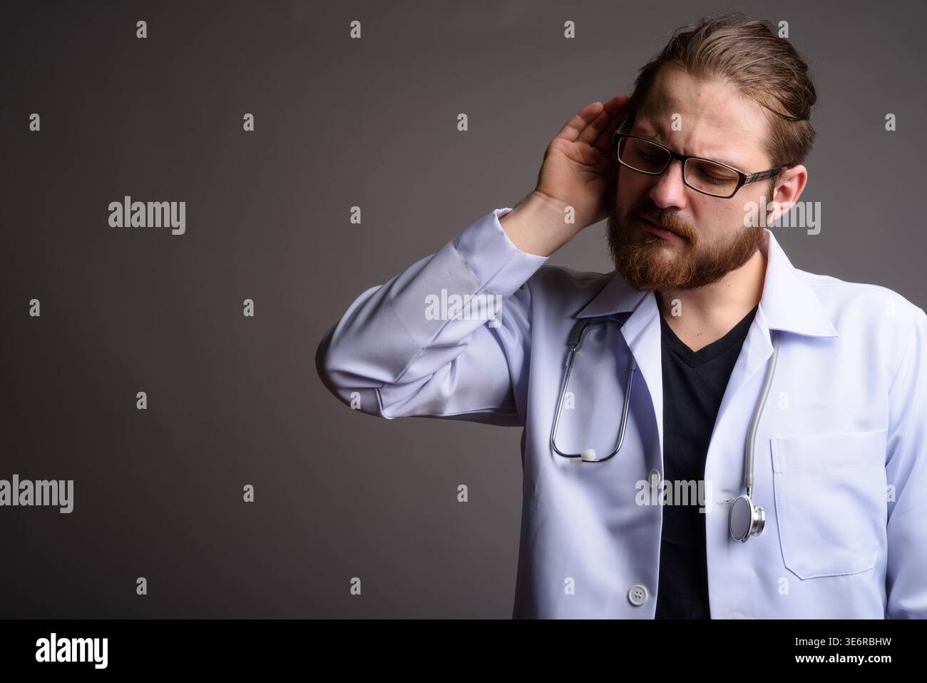 Studio portrait of a bearded young male doctor in a white lab coat with ...