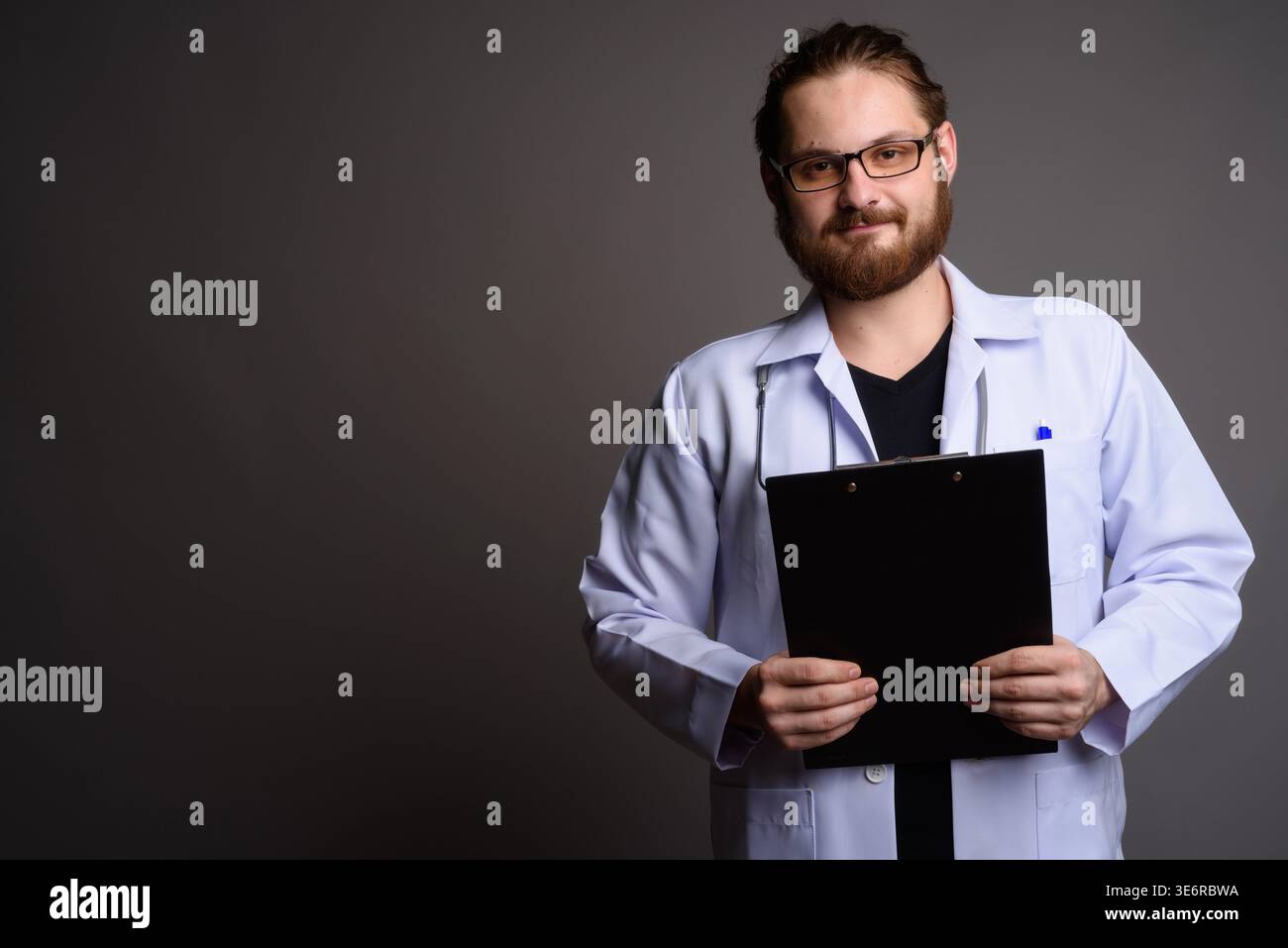 Studio portrait of a smiling bearded young male doctor in a white lab ...
