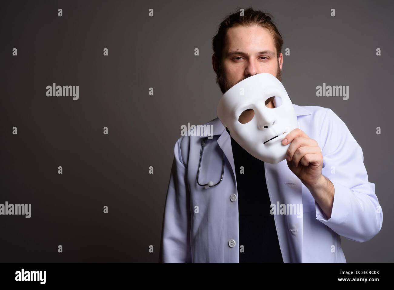 Studio portrait of a bearded young male doctor in a white lab coat with ...