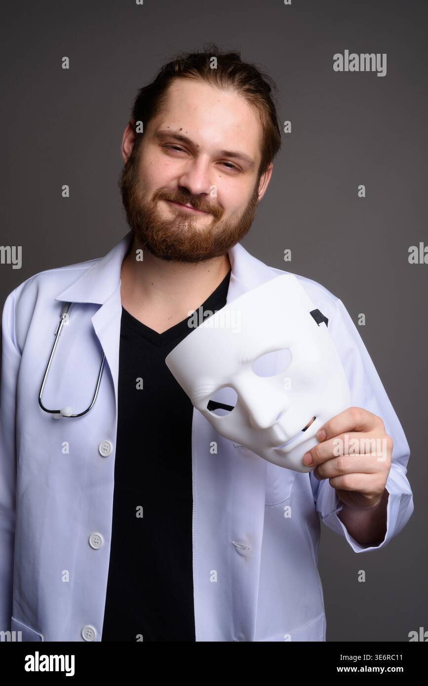 Studio portrait of a smiling bearded young male doctor in a white lab ...