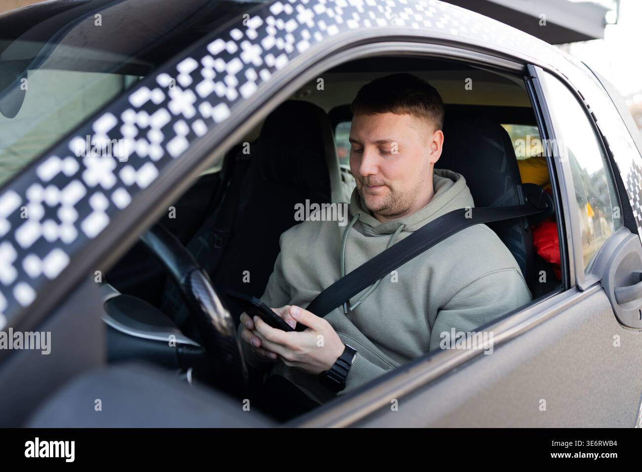 Driver using smartphone while wearing seatbelt in parked car Stock Photo