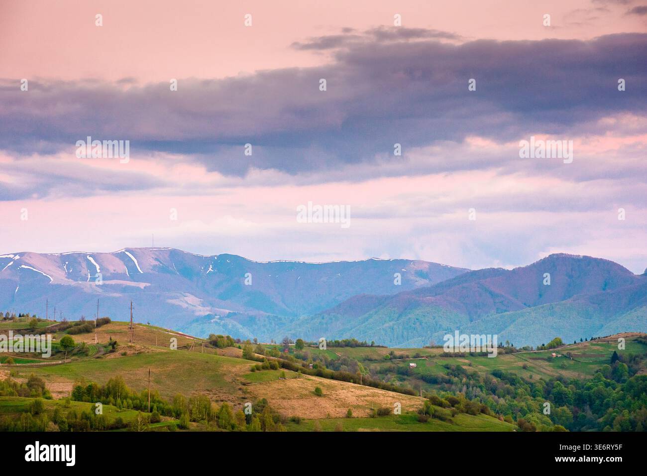 dusk over mountainous countryside scenery. dramatic sky above the distant valley and ridge. remote green meadows and trees on rolling hills. beautiful Stock Photo