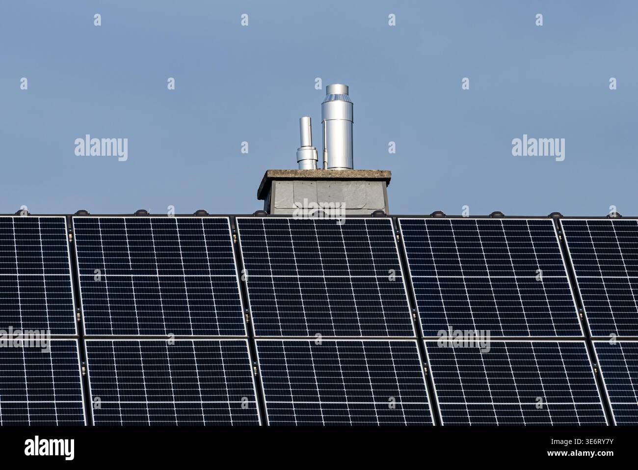 Solar panels cover a rooftop under a clear blue sky. Two metal pipes ...