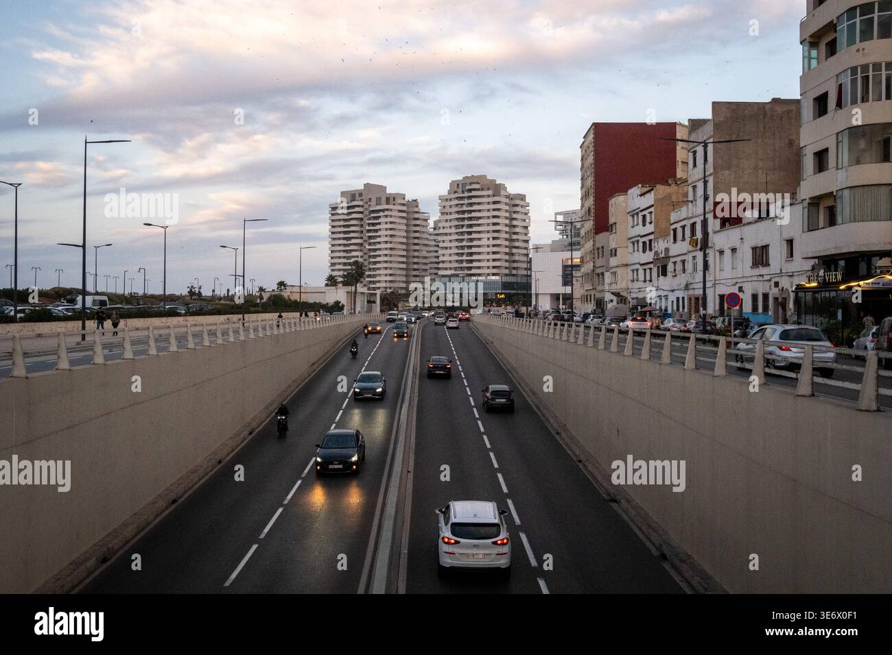 Cars drive through a sunken urban roadway bordered by apartment buildings and sidewalks in Casablanca, Casablanca-Settat, Morocco, October 18, 2023. C Stock Photo