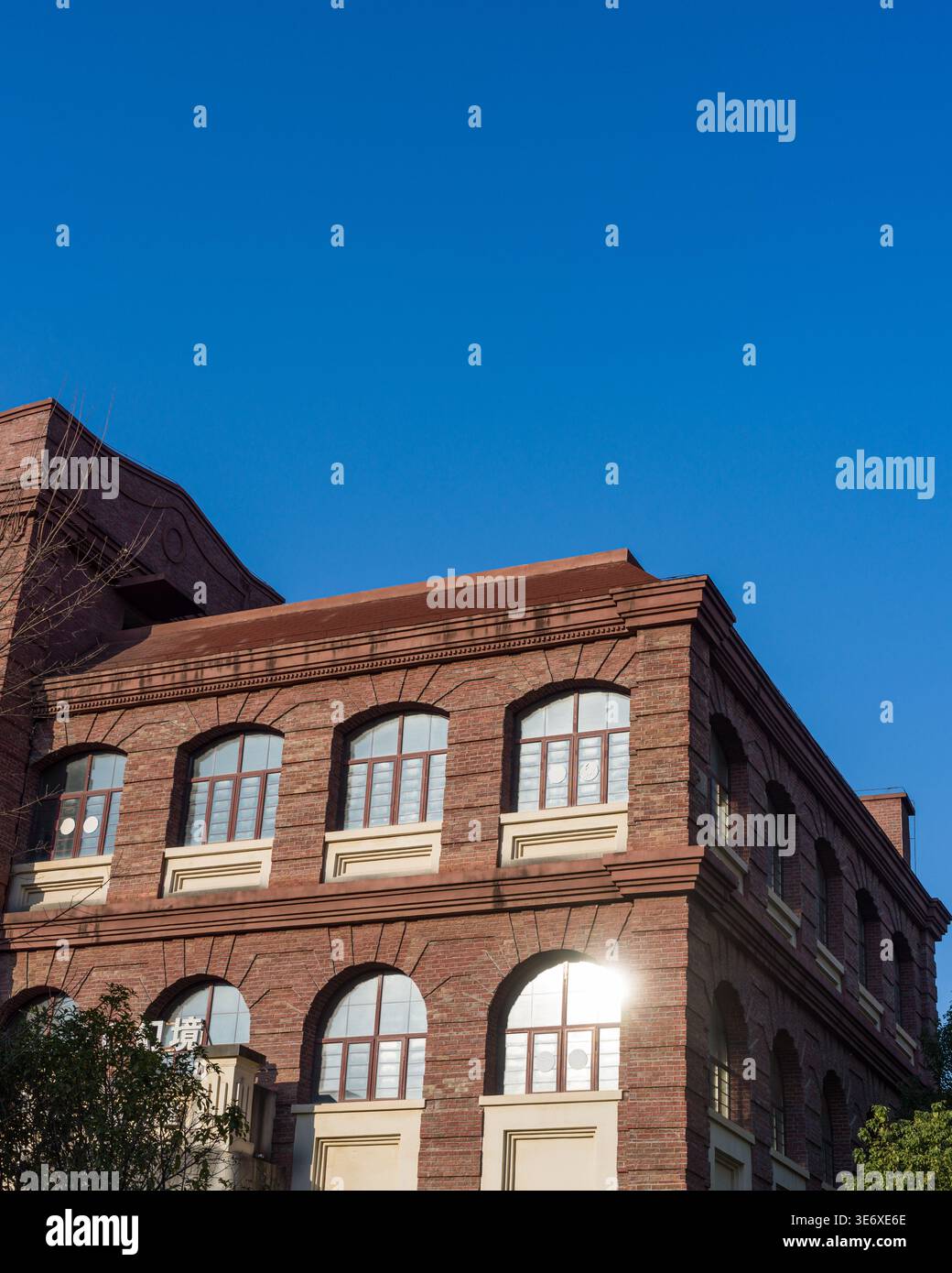 Low angle view of a classic red brick architectural facade featuring large arched glass windows reflecting bright sunlight under a clear blue sky. The Stock Photo