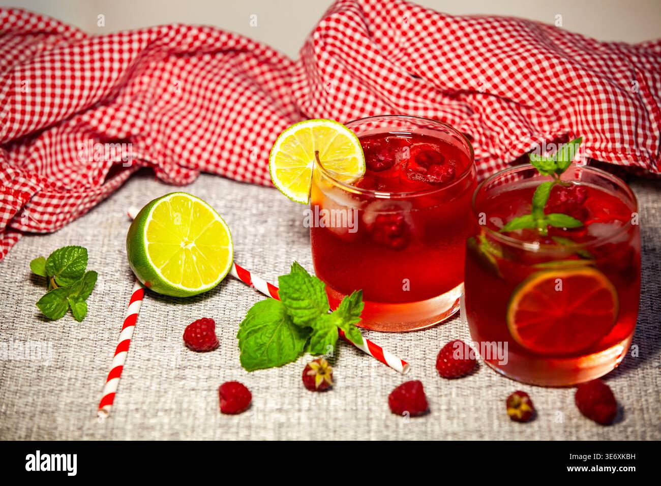Two glasses of cold red berry cocktail with fresh raspberries, lime slices and mint leaves. Summer healthy drink on a rustic background with checkered Stock Photo