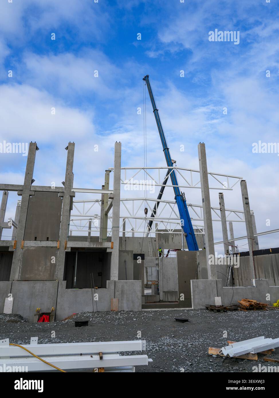 Construction crane lifts steel trusses onto concrete structure as ...