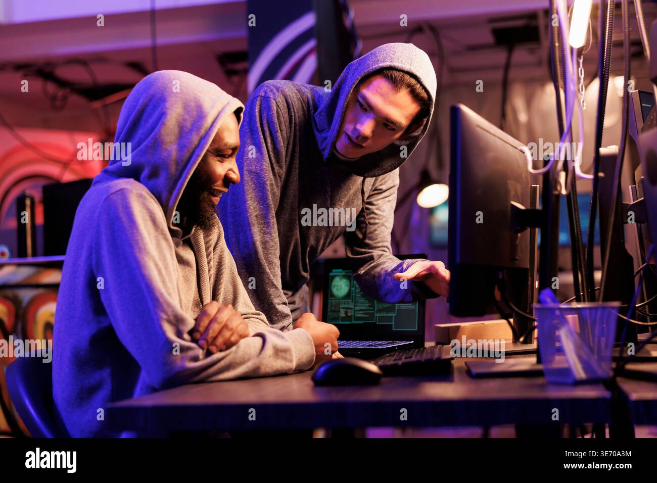 Hackers smiling while cracking encrypted information successfully on computer and working together in hideout place. Two criminals coding illegal malicious software for server hacking Stock Photo