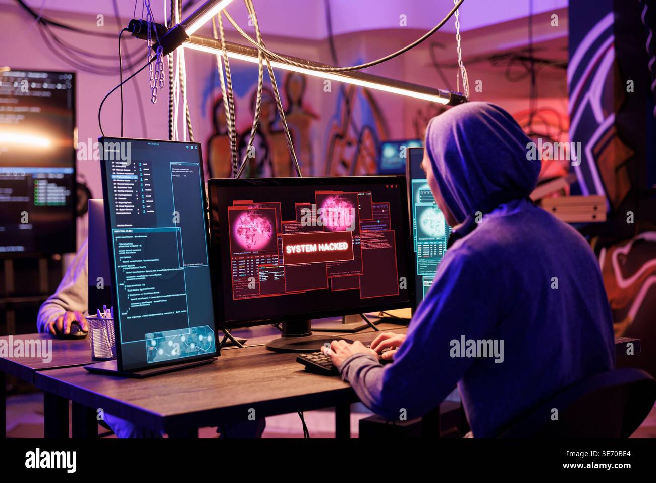 Criminal in hood successfully hacking into computer system in abandoned warehouse. Hacker gaining unauthorized access and stealing valuable data from database online server Stock Photo