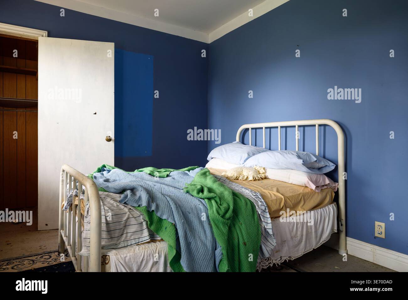A messy bed inside a blue bedroom. Stock Photo