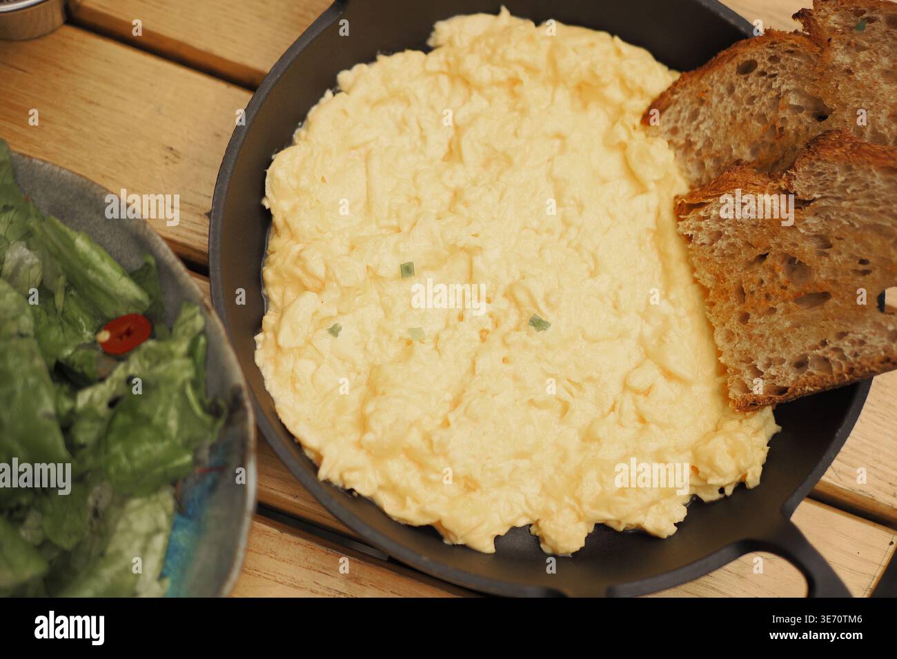 Delicious scrambled eggs served with bread and salad Stock Photo