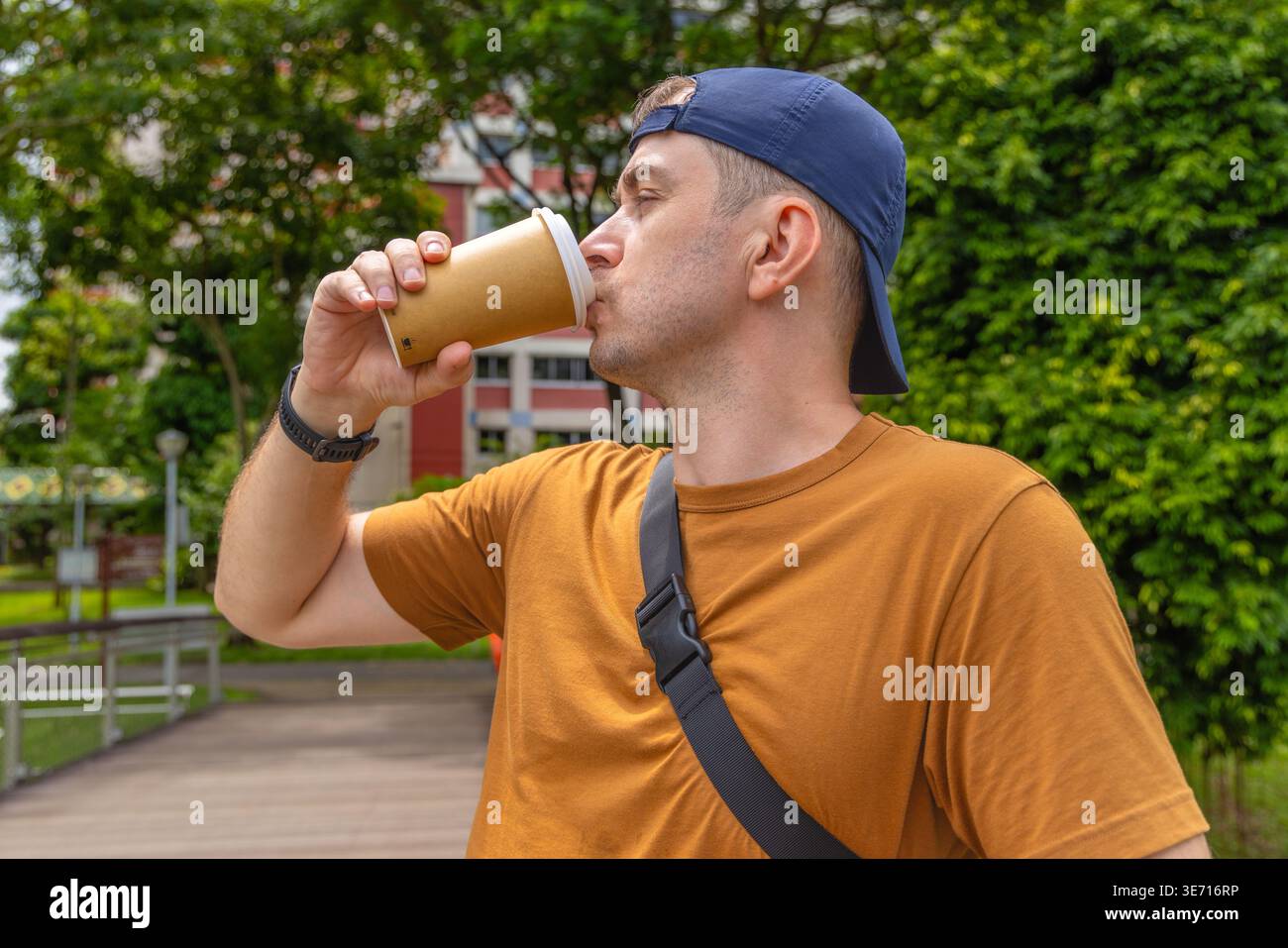 Man drinking coffee from takeaway paper cup in urban park during day shot as medium profile view Stock Photo