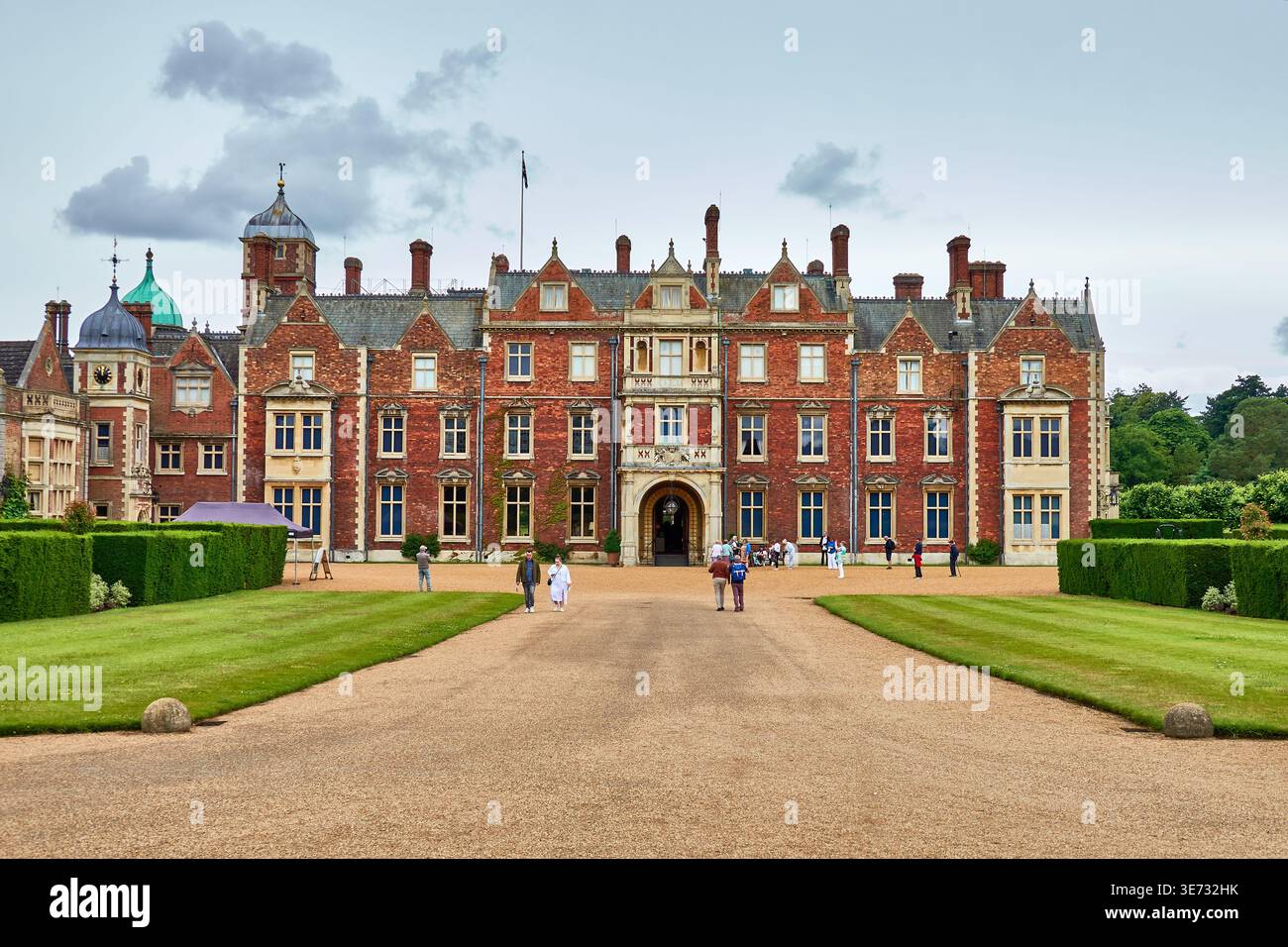 The Facade of the Royal Retreat of Sandringham House in Norfolk, England With Formal Gardens And Visitors On Gravel Driveway Stock Photo