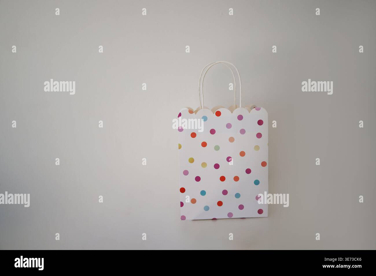 Cute polka dot gift bag on neutral background, minimal festive packaging for presents and celebrations. Stock Photo