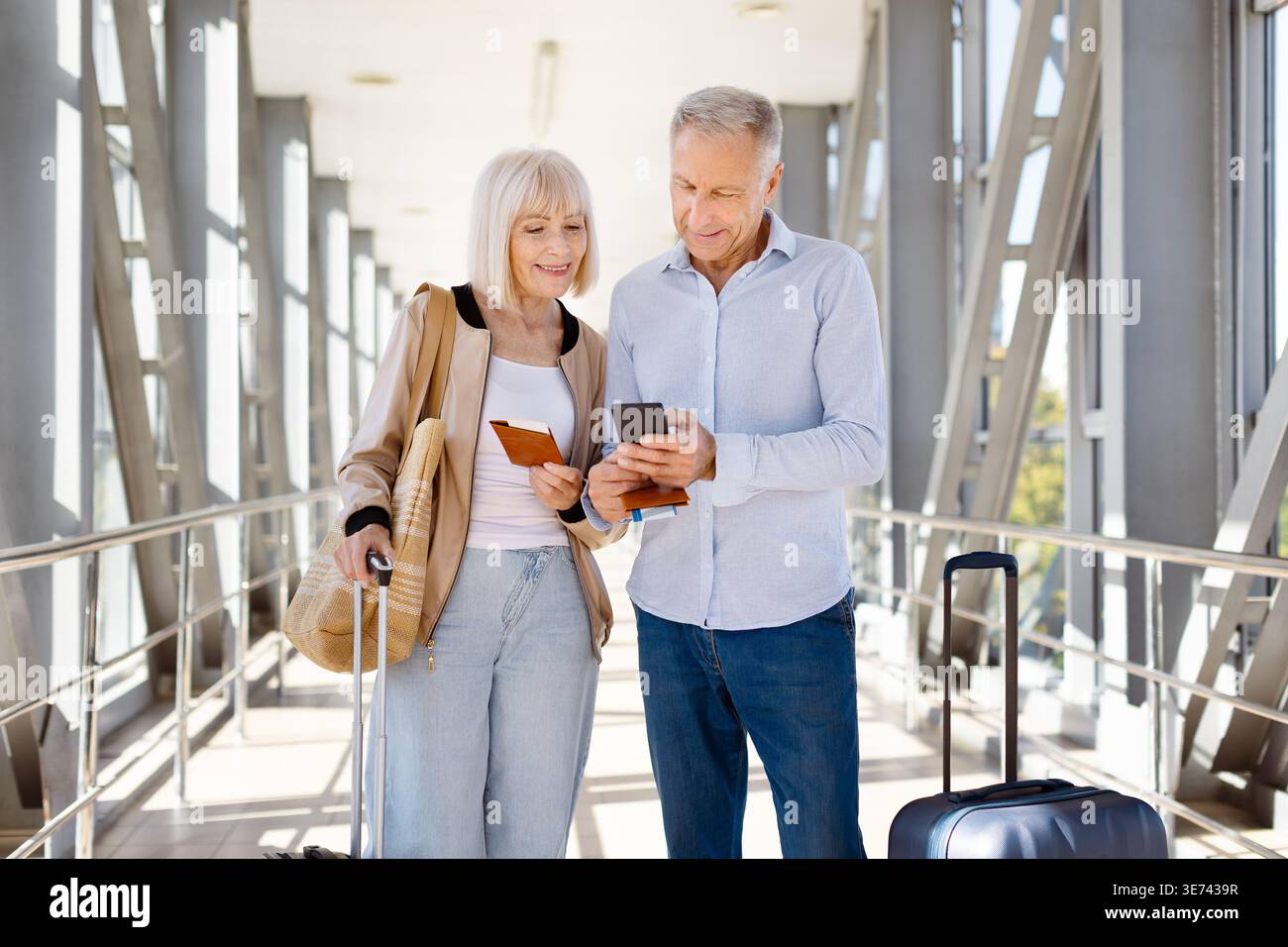 Mature couple standing in airport, man using smartphone while woman holds passport Stock Photo