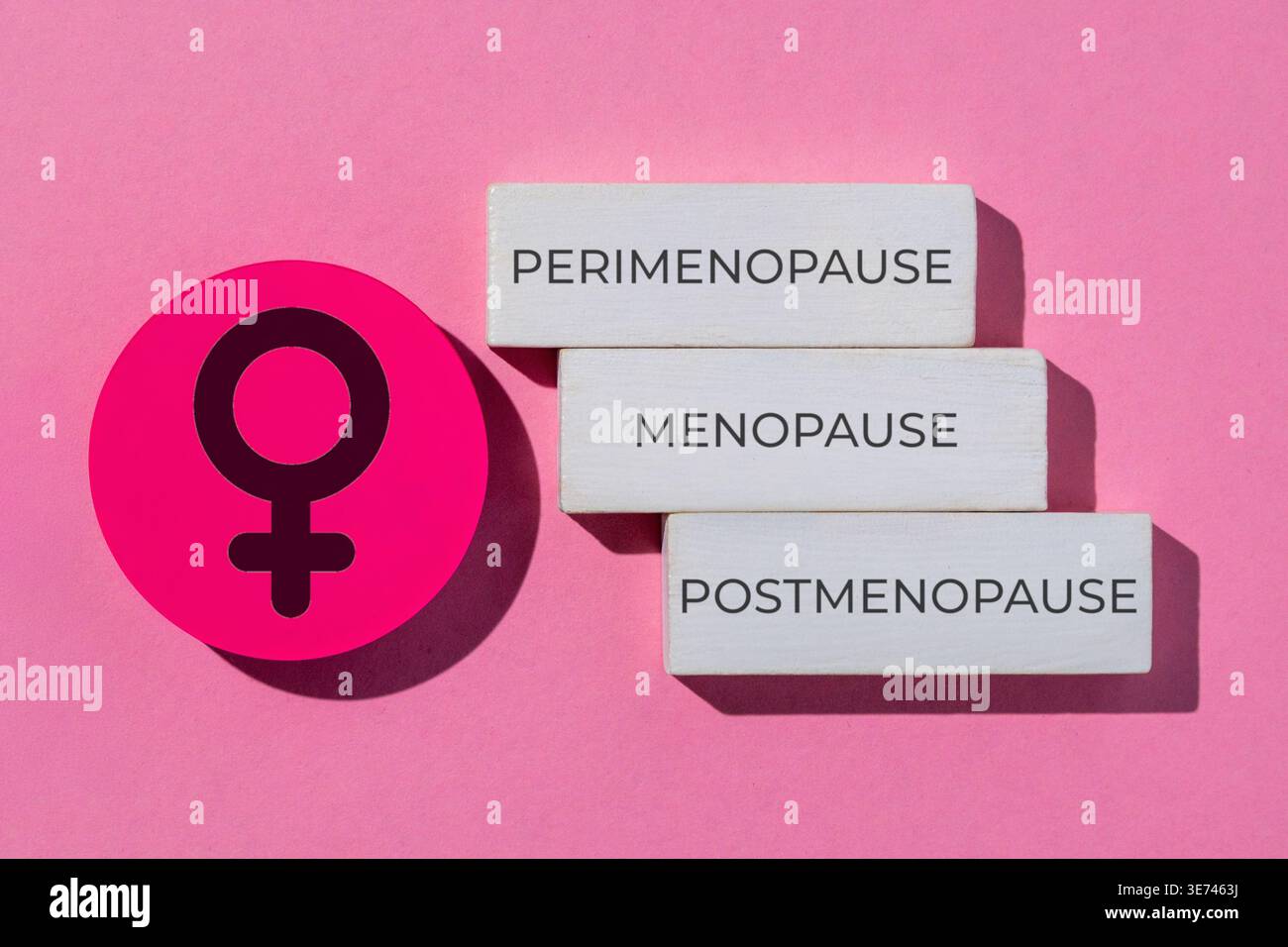 Wooden blocks labeled perimenopause, menopause, and post menopause arranged with a female symbol icon on a pink background. Stock Photo