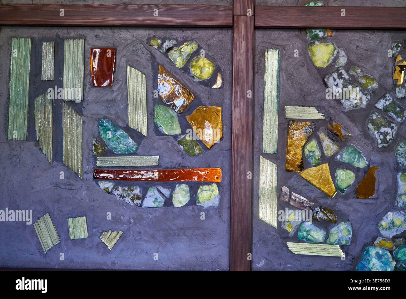 Abstract mosaic artwork featuring irregular fragments of colored glass and ceramic pieces in shades of green, amber, orange, and red, embedded in a Stock Photo