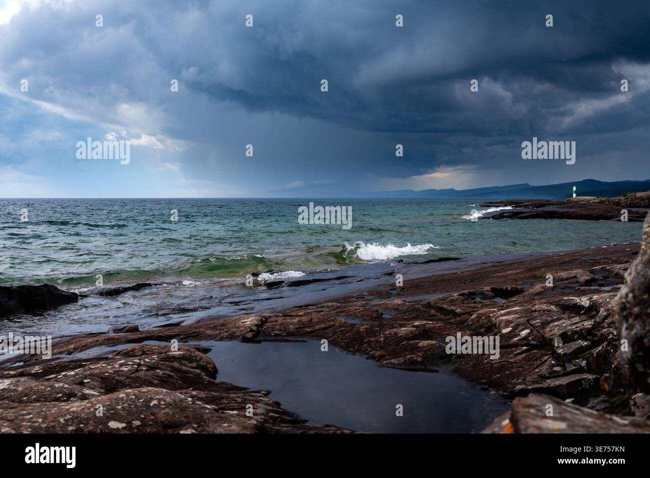 Dramatic Storm Over Rocky Coastline With Lighthouse and Rolling Waves Under Dark Clouds Stock Photo