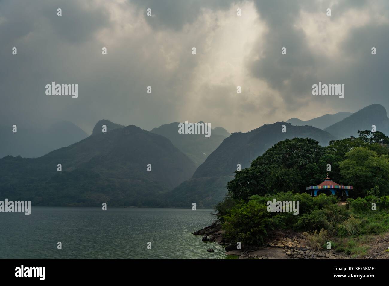 Dramatic sun rays breaking through dark storm clouds over a mountain lake Stock Photo