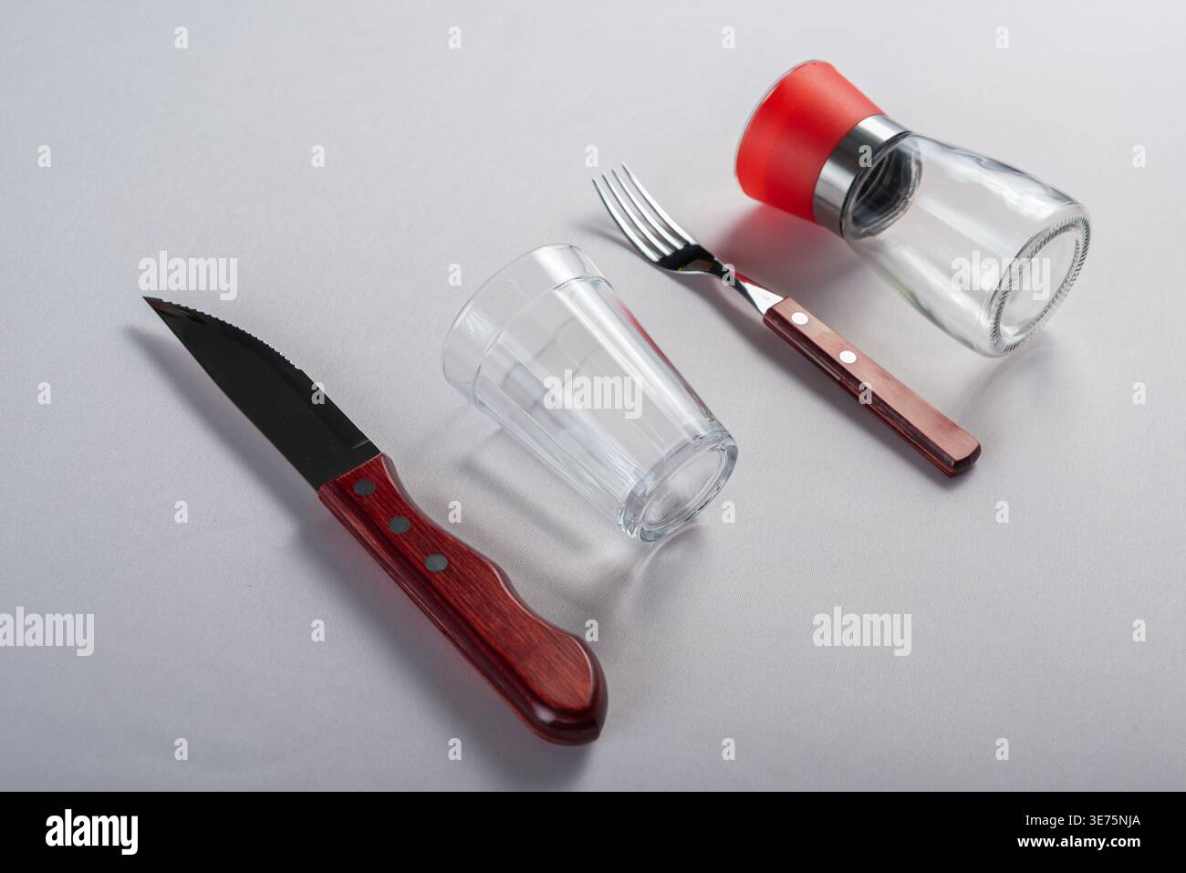 Isolated on white. Minimalist setup featuring knife, fork, glass and pepper mill. Soft diffused lighting emphasizes wood textures and clear glass. Com Stock Photo