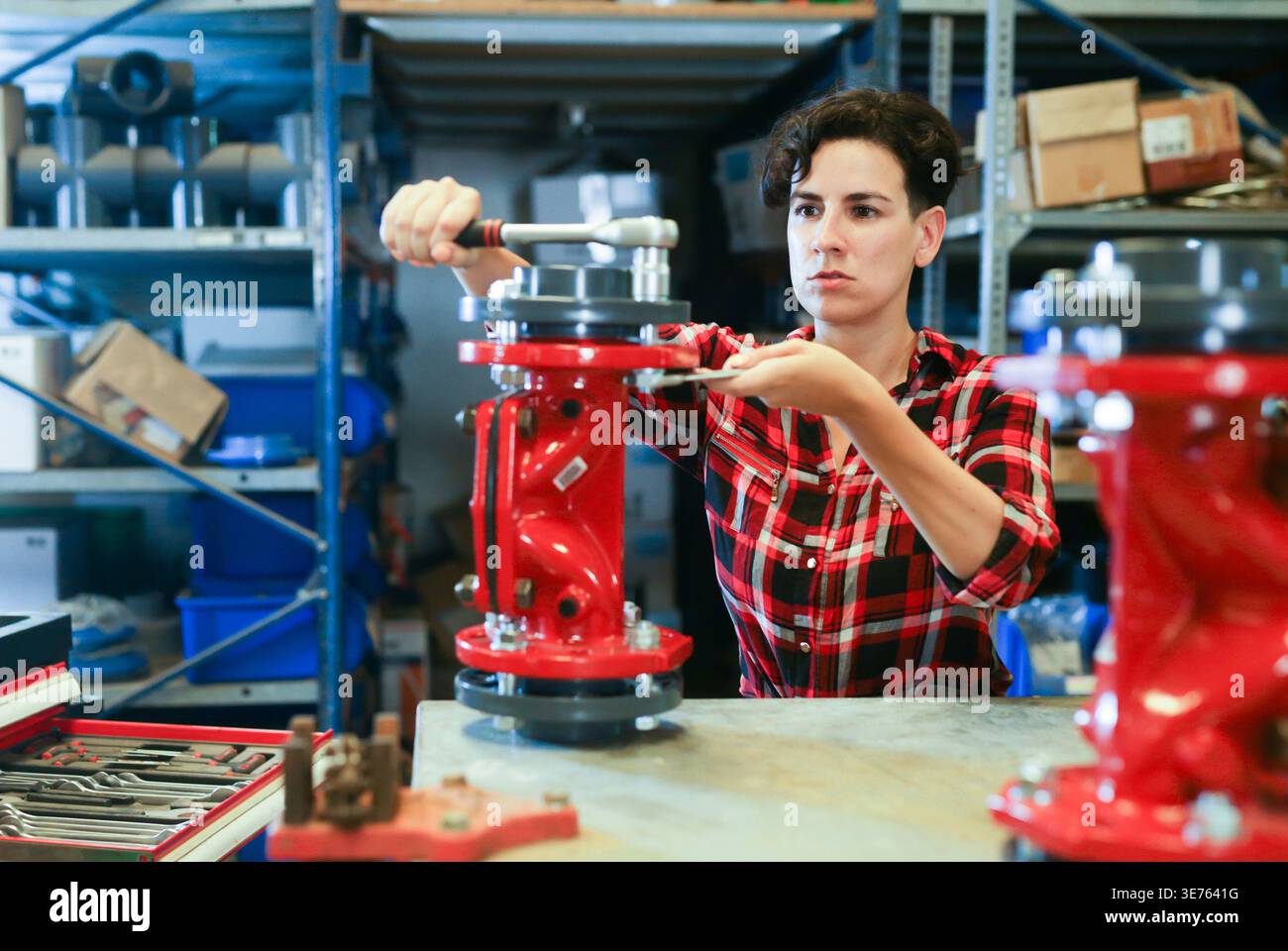 Female worker assembles shutoff valves using various tools in factory indoor Stock Photo