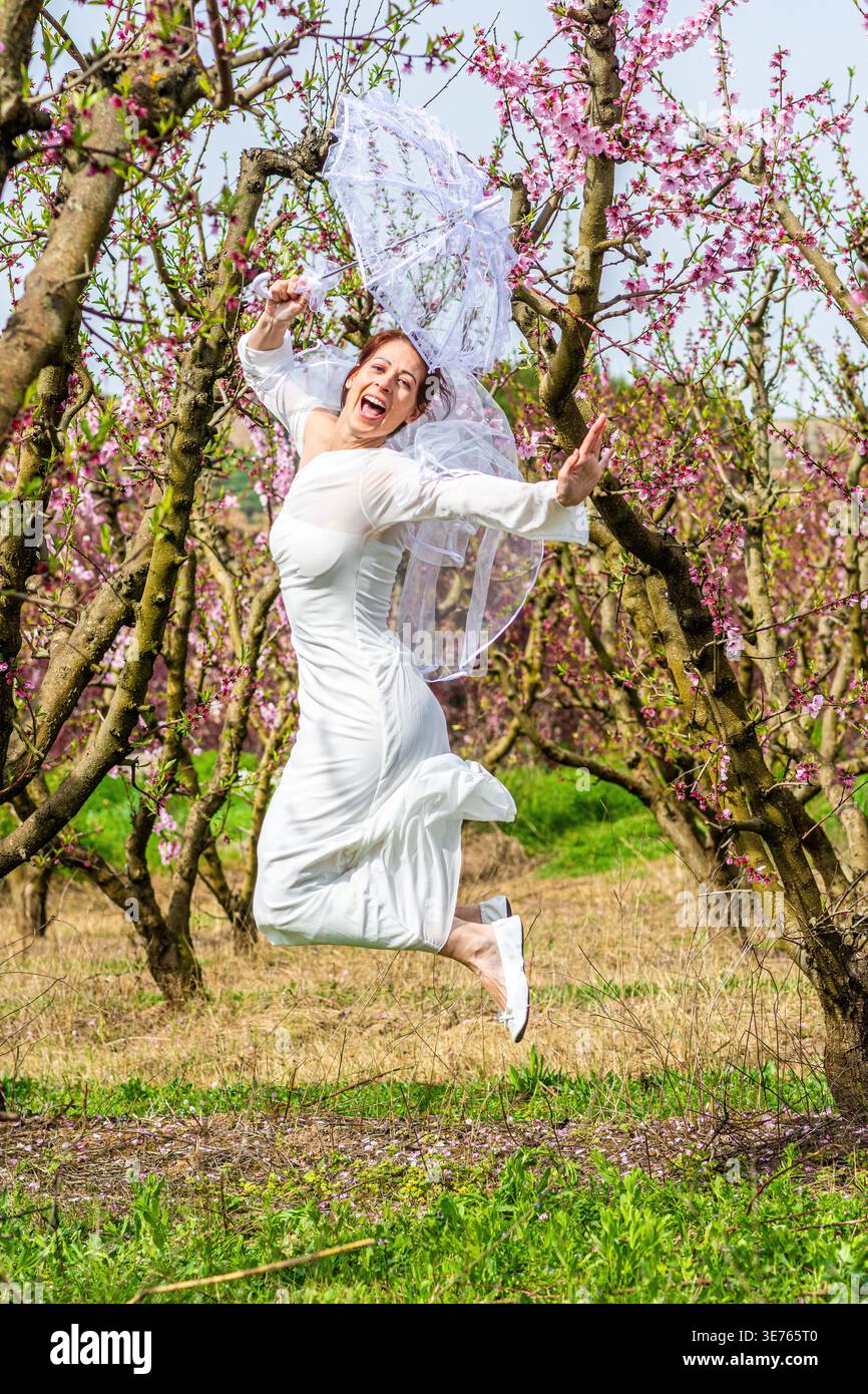 Bride joyfully jumping in blooming orchard during spring Stock Photo