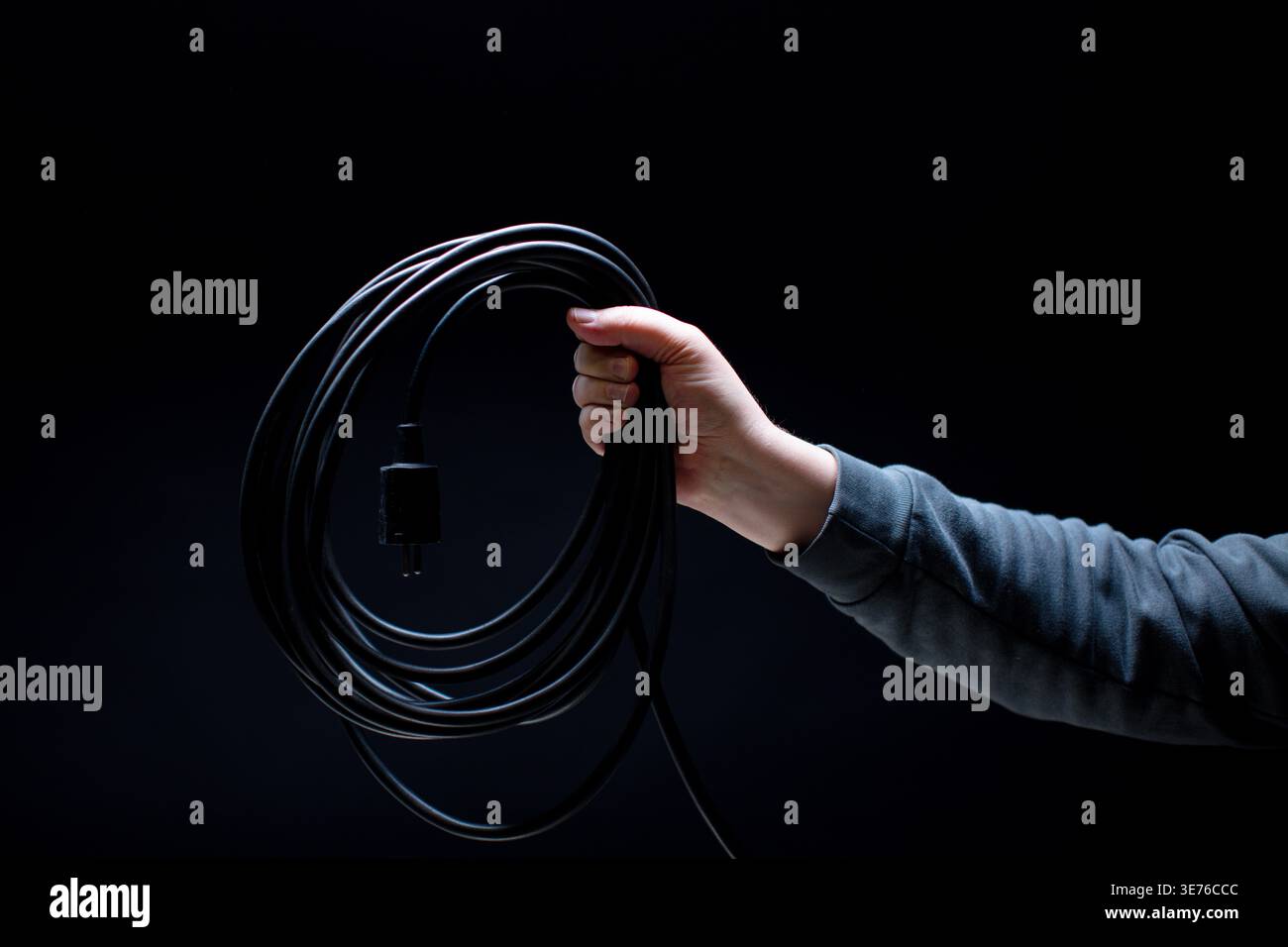 Hand holding black power cable on black background Stock Photo